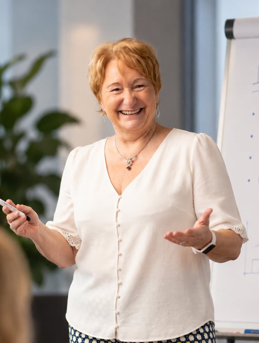 Jacqueline Cattoor, smiling with open arms, leading a session in front of a flipchart.